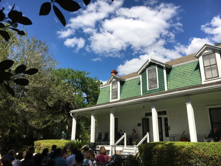 A group of wedding guests seated in front of a white house with a green roof